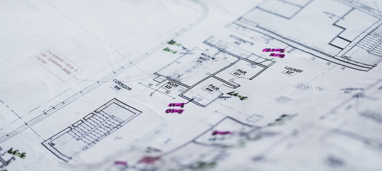 Plan architectural détaillé de l'agencement d'un bâtiment, marqué de notes manuscrites en rose et en vert pour mettre en valeur le plan et se conformer au permis d'urbanisme. Des lignes de dessin et des étiquettes indiquent les couloirs, les pièces et les entrées.