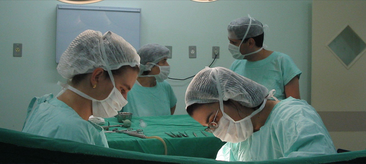 Des chirurgiens en tenue d'hôpital et masqués effectuent une opération dans une salle d'opération animée, incarnant la précision des réseaux hospitaliers. Deux chirurgiens se concentrent intensément sur la procédure tandis que deux autres membres du personnel médical observent et discutent, avec des outils médicaux essentiels soigneusement disposés sur une table à proximité.